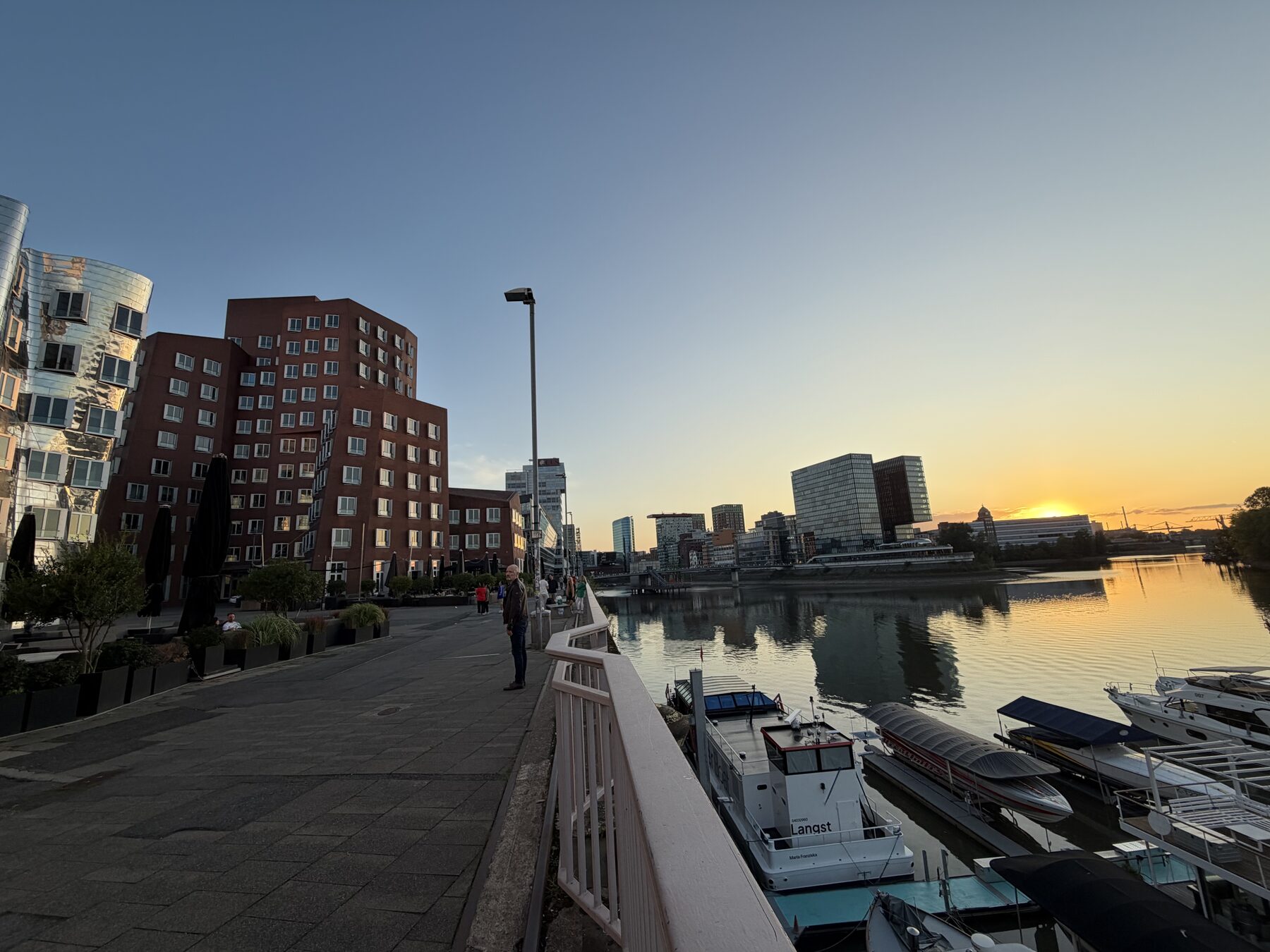 Der Düsseldorfer Medienhafen am Abend, Blick über das Wasser auf die Gehry-Bauten und die Skyline im Sonnenuntergang.