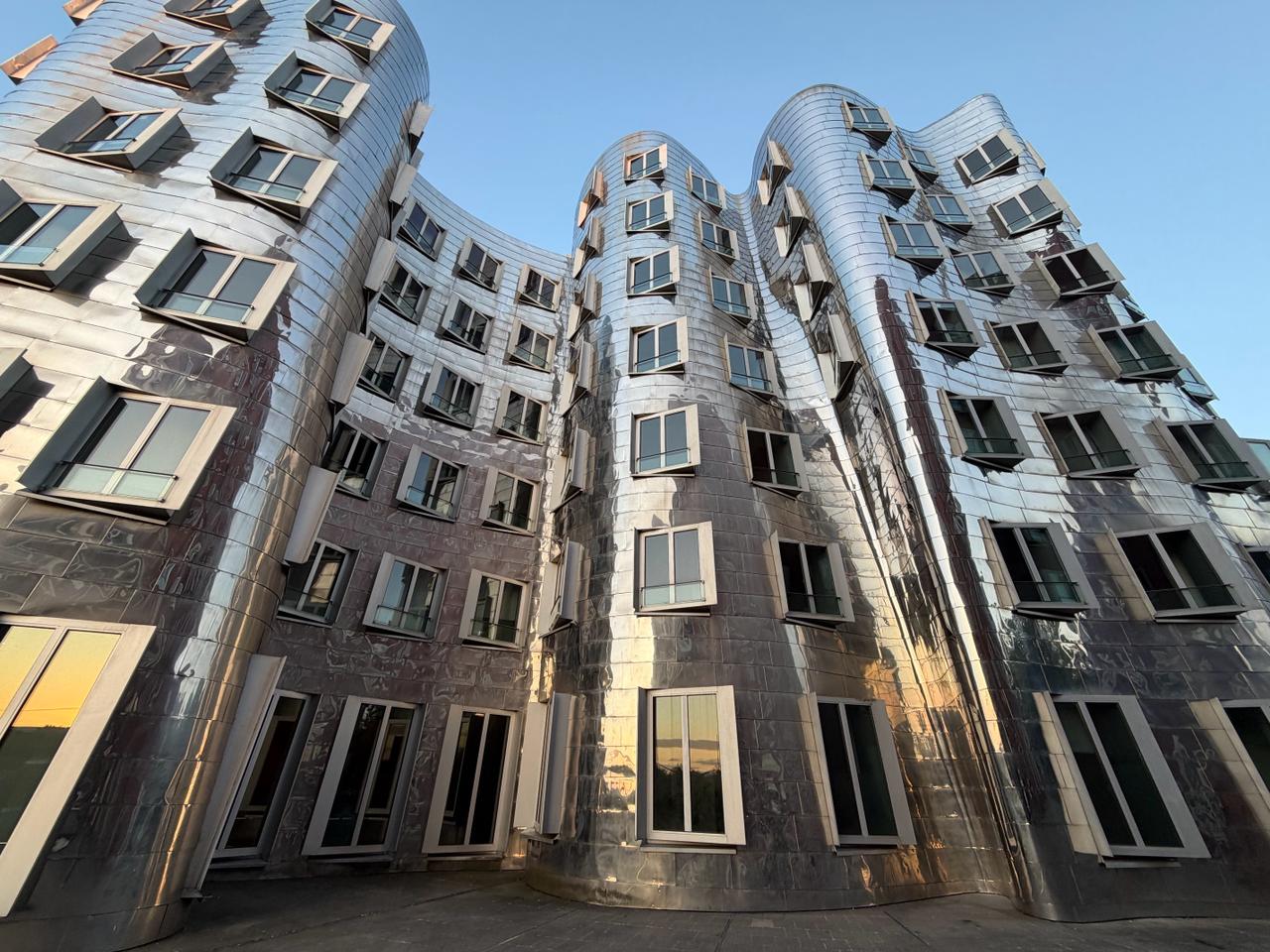 Die geschwungenen Edelstahlfassaden der Gehry-Bauten im Düsseldorfer Medienhafen im Abendlicht.